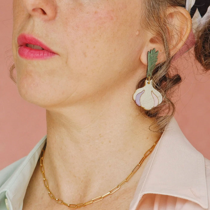 Modelo con pendientes de metacrilato en tonos marfil, malva, rosa palo, verde y dorado en forma de cabeza de ajos.