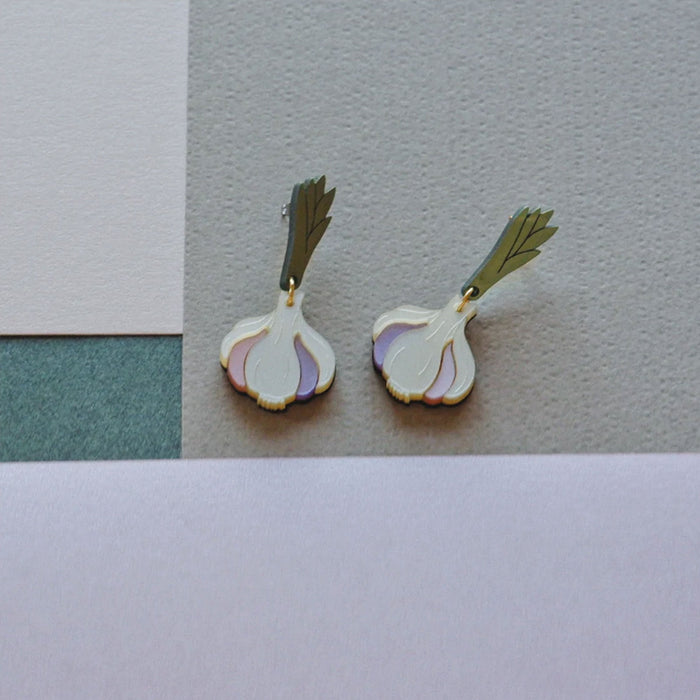 pendientes de metacrilato en tonos marfil, malva, rosa palo, verde y dorado en forma de cabeza de ajos sobre fondo en tonos grises