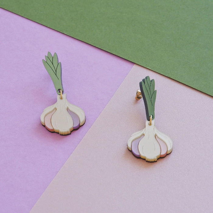 pendientes de metacrilato en tonos marfil, malva, rosa palo, verde y dorado en forma de cabeza de ajos sobre fondo en tonos malva, rosa palo y verde