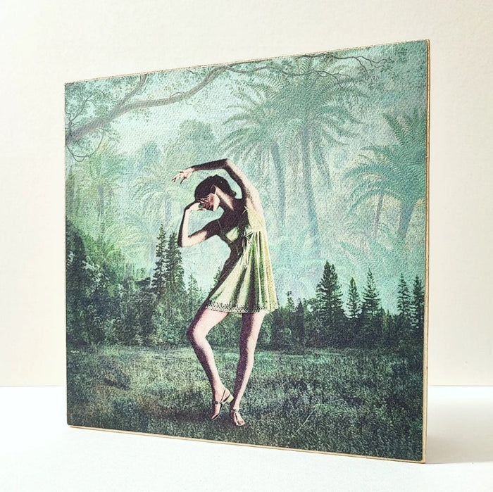 Caja de luz de madera y papel con la imagen de una bailarina frente a un bosque. Mientras está apagada sólo aparece la bailarina y el fondo vegetal, cuando está encendida aparece en la parte superior de la imagen la palabra "bella". Caja de luz hecha de forma manual.