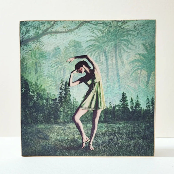 Caja de luz de madera y papel con la imagen de una bailarina frente a un bosque. Mientras está apagada sólo aparece la bailarina y el fondo vegetal, cuando está encendida aparece en la parte superior de la imagen la palabra "bella". Caja de luz hecha de forma manual.