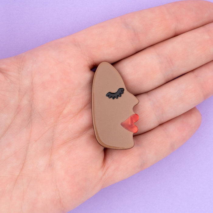 Pasador para el pelo en forma de cara negra de perfil con labios rojos y pestañas largas negras.