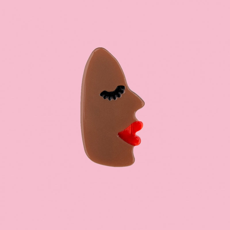Pasador para el pelo en forma de cara negra de perfil con labios rojos y pestañas largas negras.