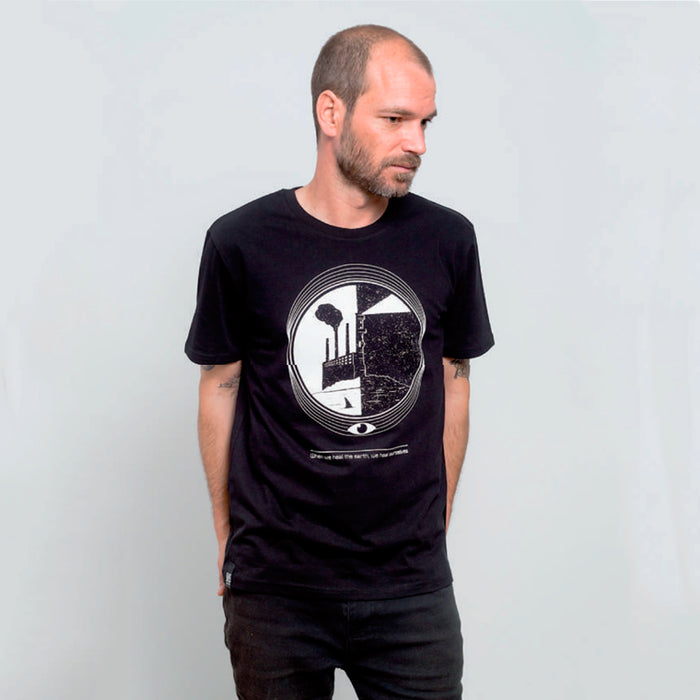 Camiseta negra con ilustración en circular de una fábrica con chimenea junto al a playa y un faro iluminando el cielo nocturno junto con el texto "When we heal the earth we heal ourselves", todo en tonos blancos.