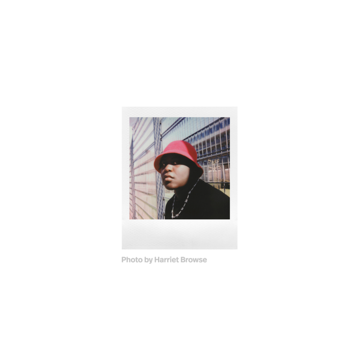 Fotografia polaroid go de una persona negra con gorro rojo ante una valla tomada por Harriet Browse