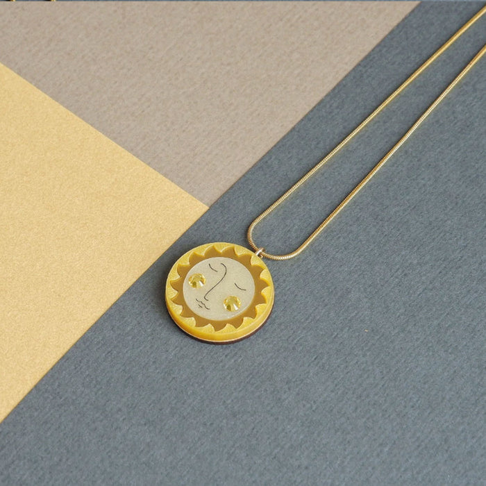 Collar con colgante redondo en forma de sol en tonos dorados y amarillos con mejillas de crital de swarovski y cadena dorada de acero inoxidable hipoalergénico.