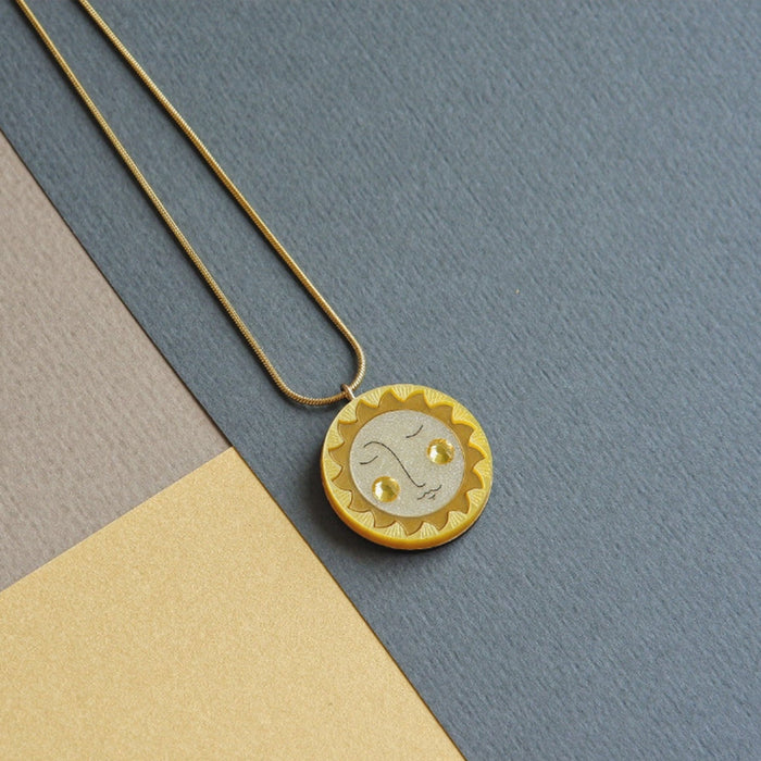 Collar con colgante redondo en forma de sol en tonos dorados y amarillos con mejillas de crital de swarovski y cadena dorada de acero inoxidable hipoalergénico.