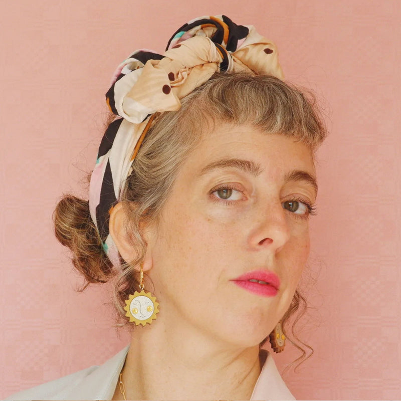 Pendientes de aro con charm de metacrilato en forma de sol con rostro y cristal de swarovski en las mejillas en plano de medio lado