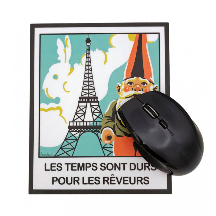 Alfombrilla de ratón rectangular con dibujo de gnomo de jardín ante la torre Eiffiel y una nube en forma de conejo dentro de un marco de foto tipo Polaroid. Alfombrilla para ratón inspirada en la película Amelie con el texto "Les temps sont durs pour les rêveurs". Con ratón sobre ella.