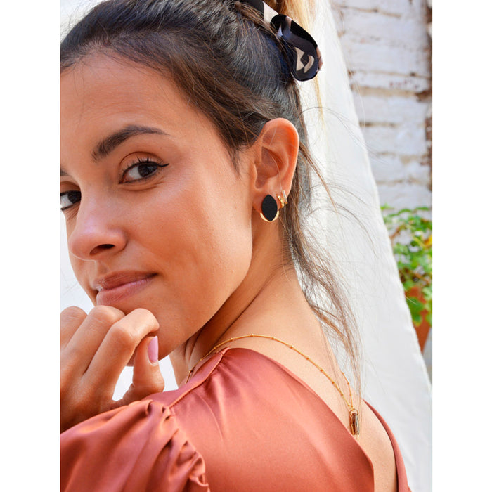 Modelo llevando pendientes de madera con forma de hoja de olivo en color negro y semicírculo dorado en la parte inferior trasera.