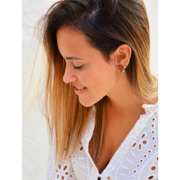 Modelo llevando Pendientes de madera con forma de hoja de olivo en color terracota y semicírculo dorado en la parte inferior trasera.