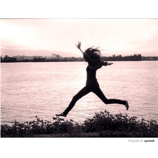 Fotografía en banco y negro tomada con la película Kodak  Trix  ISO  400  de una chica saltando en un camino con hierba junto a un rio