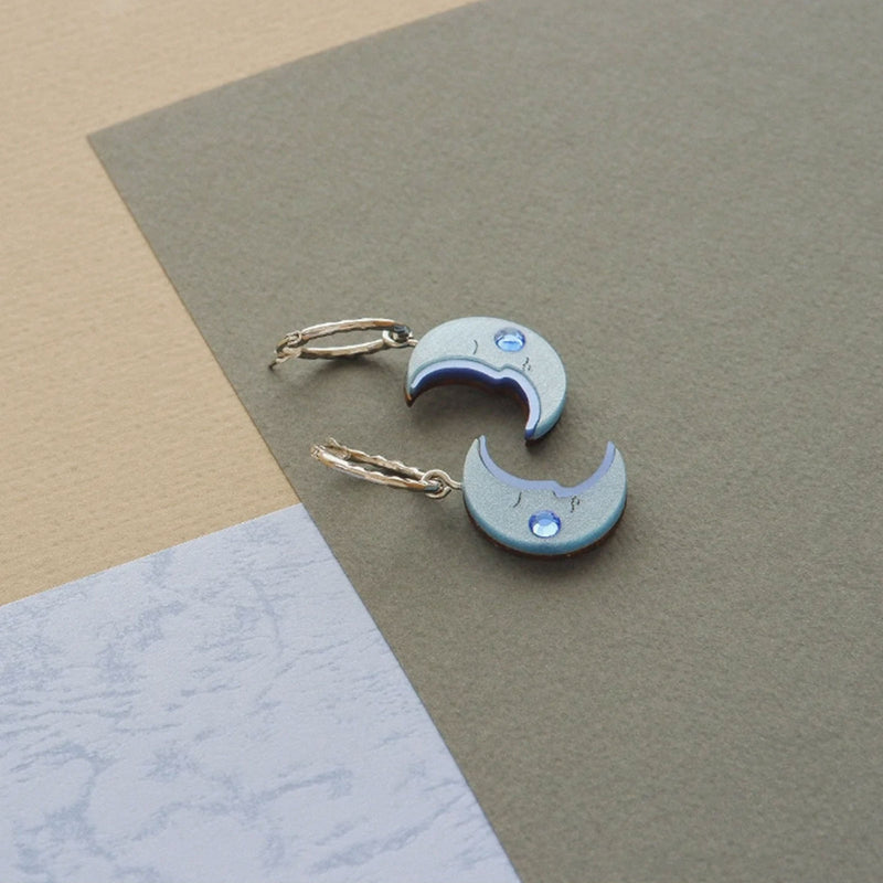 Pendientes de aro plateado con charm en forma de media luna azul con mejillas de cristal de swarovski sobre fondo de colores tierra y azules