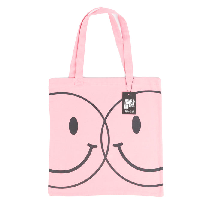 Tote bag color rosa con serigrafía de dos caritas sonrientes tipo smiley en color negro en una cara.