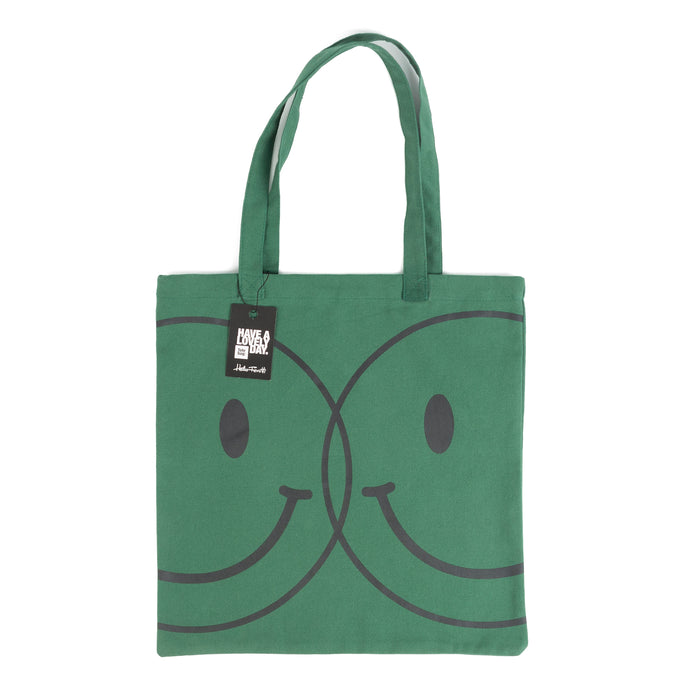 Tote bag color verde con serigrafía de dos caritas sonrientes tipo smiley en color negro en una cara.