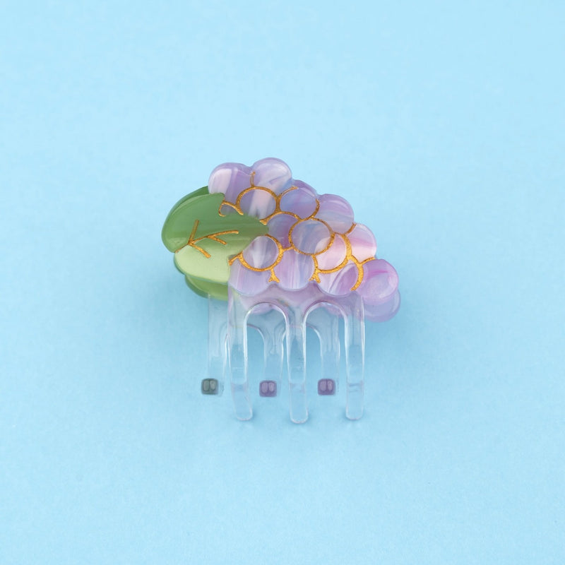 Pinza mini para el pelo en forma de racimo de uvas. Pinza original y divertida fabricada con acetato de celulosa reciclado y biodegradable. Vista lateral sobre fondo plano.