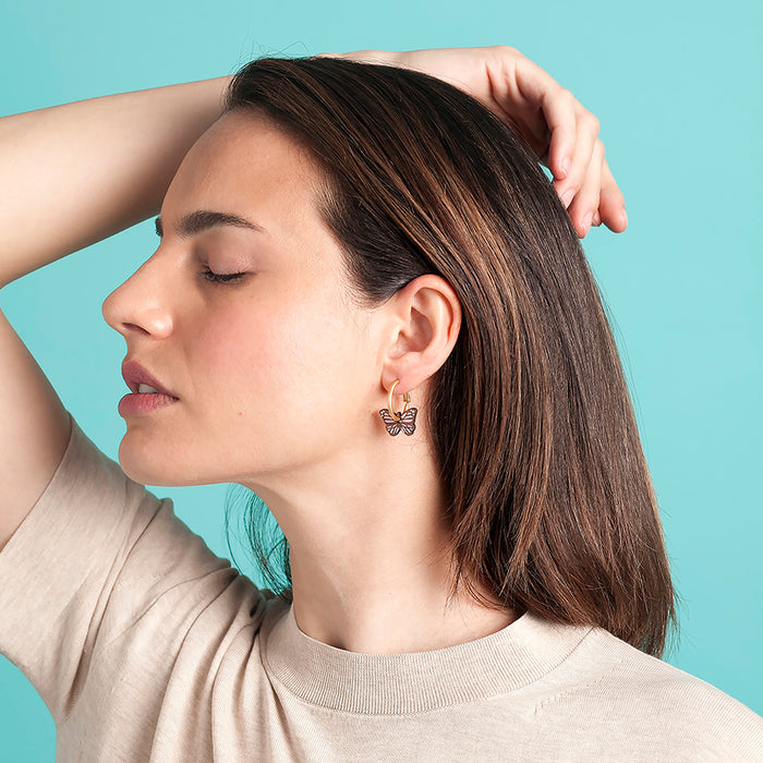 Modelo con Pendientes de aro con charm de madera en forma de mariposa con detalles pintados en morado