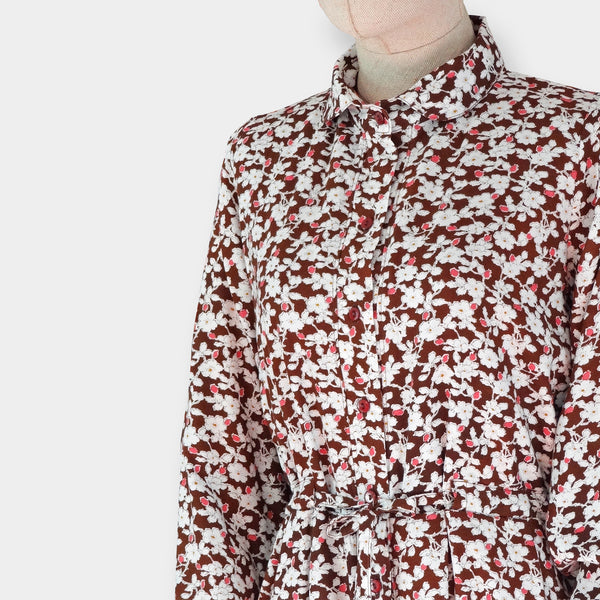Vestido camisero de manga larga teja y estampado de flores blancas y rosas, con cinturón del mismo tejido, forro interior en el cuerpo, bolsillos, botonadura frontal y cinturón interior. 