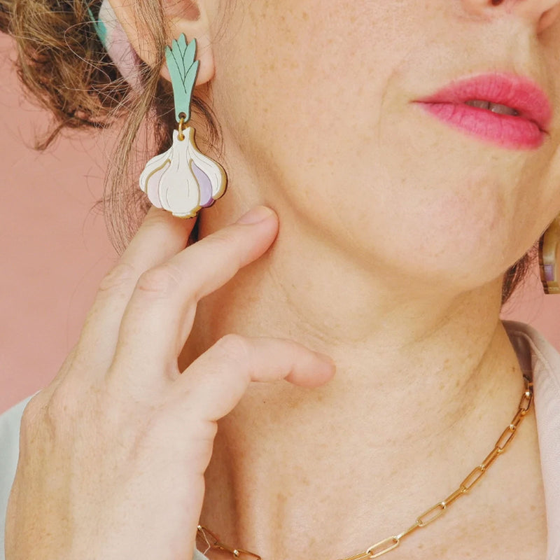Modelo con pendientes de metacrilato en tonos marfil, malva, rosa palo, verde y dorado en forma de cabeza de ajos.