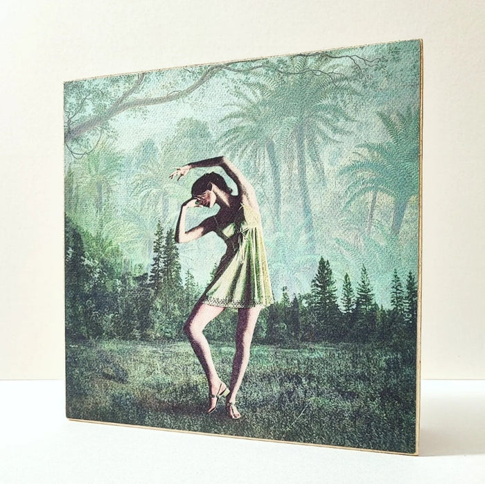 Caja de luz de madera y papel con la imagen de una bailarina frente a un bosque. Mientras está apagada sólo aparece la bailarina y el fondo vegetal, cuando está encendida aparece en la parte superior de la imagen la palabra "bella".  Caja de luz hecha de forma manual.