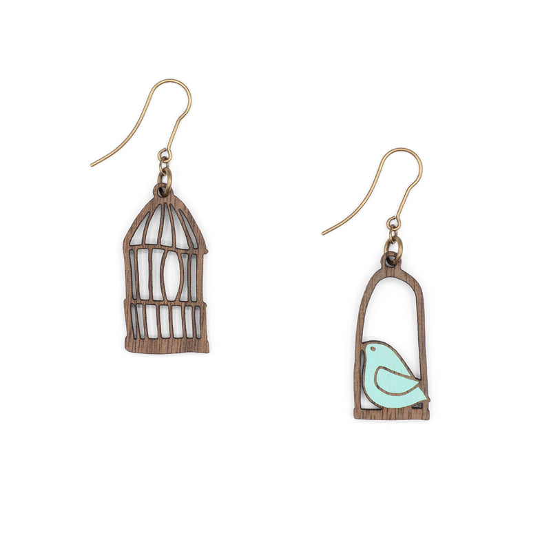 Pendientes desparejados en forma de pájaro azul en un columpio y jaula de pájaro sobre fondo blanco.