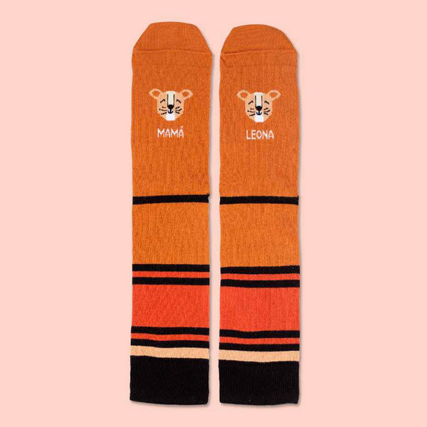 Calcetines divertidos de tonos anaranjados, rayas negras, dibujos de caras de leona y el texto "mamá" y "leona". 