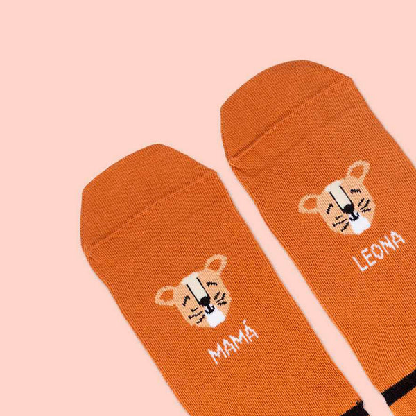Detalle de calcetines divertidos de tonos anaranjados con los dibujos de dos caras de lona y el texto "mamá" y "leona" en cada uno.