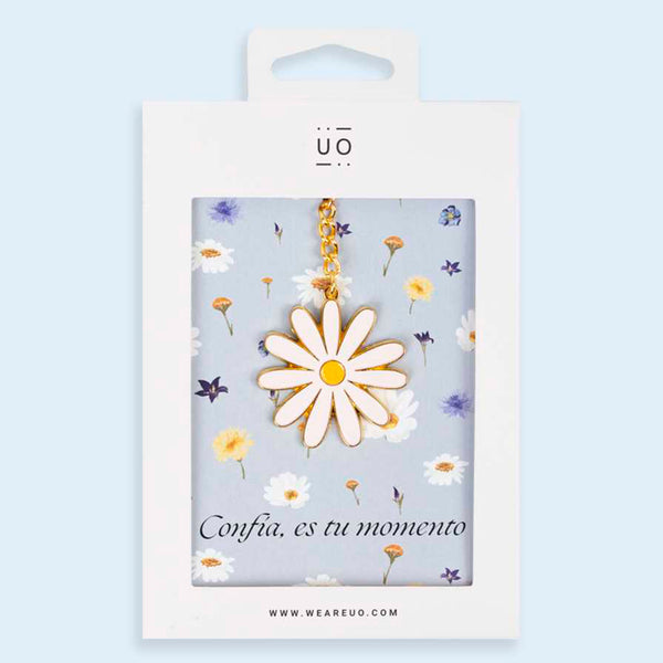 Llavero de metal dorado en forma de flor margarita con hojas blancas. Packaging con fondo azul pastel de estampado de flores con el texto "Confia, es tu momento":