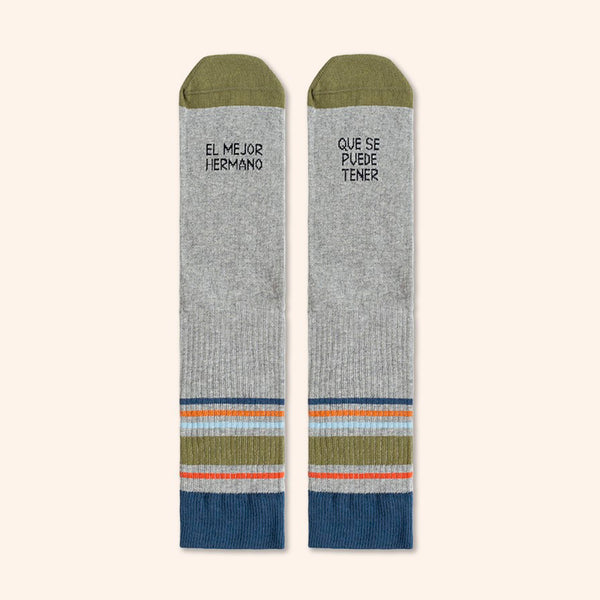 Calcetines en color gris con rayas en tonos verdes, azules y naranjas y la frase “El mejor hermano | que se puede tener” en el empeine. Calcetines grises con mensaje y puntera de color verde. 