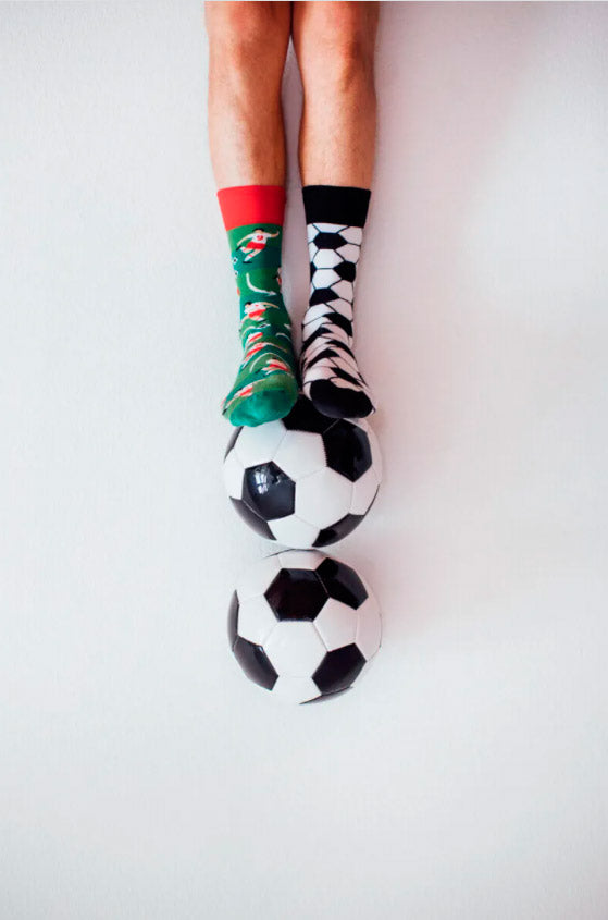 Calcetines desparejados con estampado de futbolistas jugando en el campo de fútbol y estampado imitando un balón de fútbol.