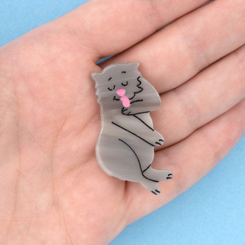 Pinza para el pelo en forma de gato gris lamiéndose una pata. Pinza para el pelo en forma de gato aseándose, divertida y original. Fabricada con acetato de celulosa reciclado. Vista sobre mano.