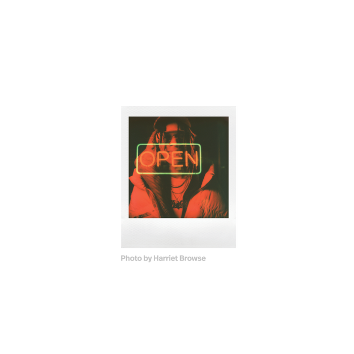 Fotografia de doble exposición polaroid go de unam ujer con chaqueta, gorra y gafas en todos rojos y un cartel de neon con el texto open tomada por Harriet Browse