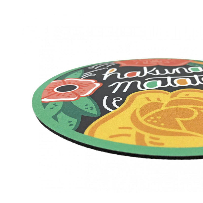 Alfombrilla de ratón redonda con fondo negro, borde verde y dibujo de flores y hojas y el texto "Hakuna Matata". Alfombrilla para ratón inspirada en El Rey León.