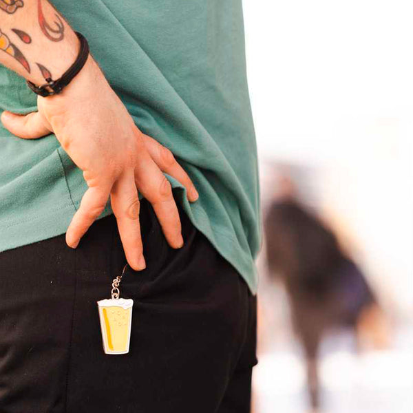 Fotografía de plano detalle del bolsillo delantero del pantalón de un hombre con un llavero en forma de vaso de cerveza sobresaliendo.