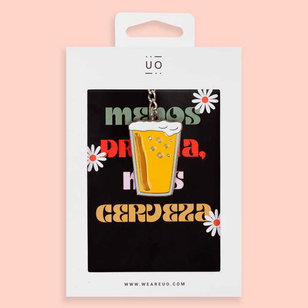 Packagind de llavero de metal plateado con charm en forma de vaso de cerveza y postal trasera con el texto "menos drama, más cerveza" sobre fondo rosado.