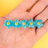 Pasador de pelo en forma de fila de flores nomeolvides azules con detalles en blanco y amarillo. Fabricado en acetato de celulosa reciclado. Vista sobre mano.