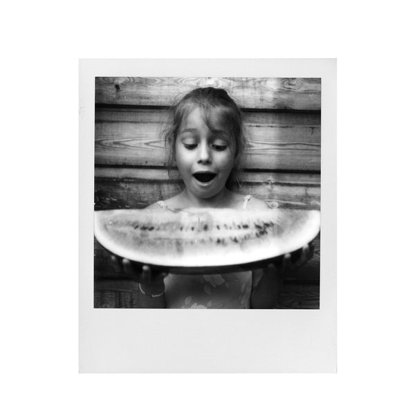 Fotografia polaroid 600 en blanco y negro de una niña asombrada ante un trozo de melon