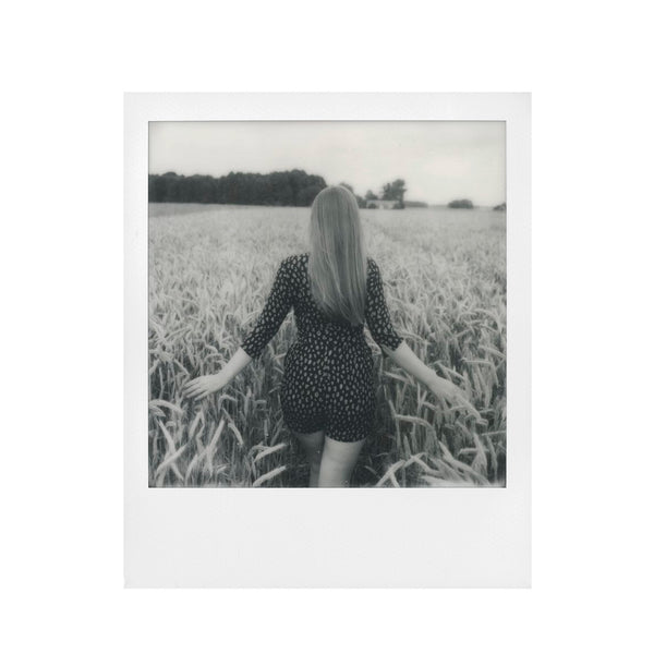 Fotografia polaroid 600 en blanco y negro de mujer de espaldas en un campo de trigo