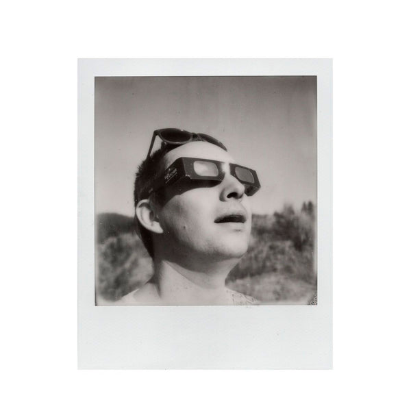 Fotografía Polaroid SX-70 de hombre blanco en primer plano mirando a lo lejos con unas gafas para eclipse solar