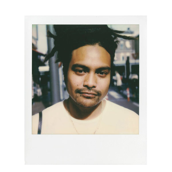 Fotografía polaroid 600 a color de un hombre racializado con piercings en un fondo urbano
