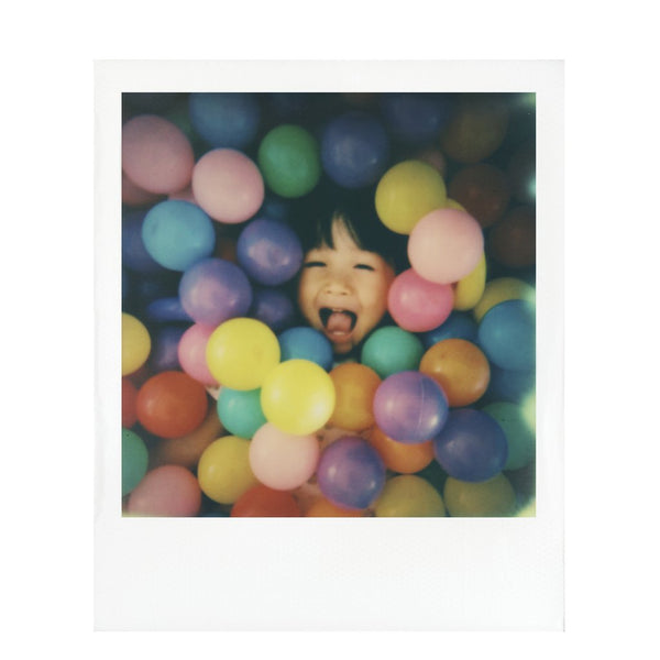 Fotografia polaroid 600 a color de una niña sonriente en una piscina de bolas