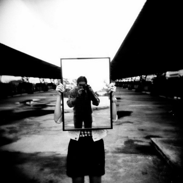 Fotografía en blanco y negro de un hombre fotografiándose en un espejo en un aparcamiento tomada con la película Fomapan Profi Line Classic ISO 100