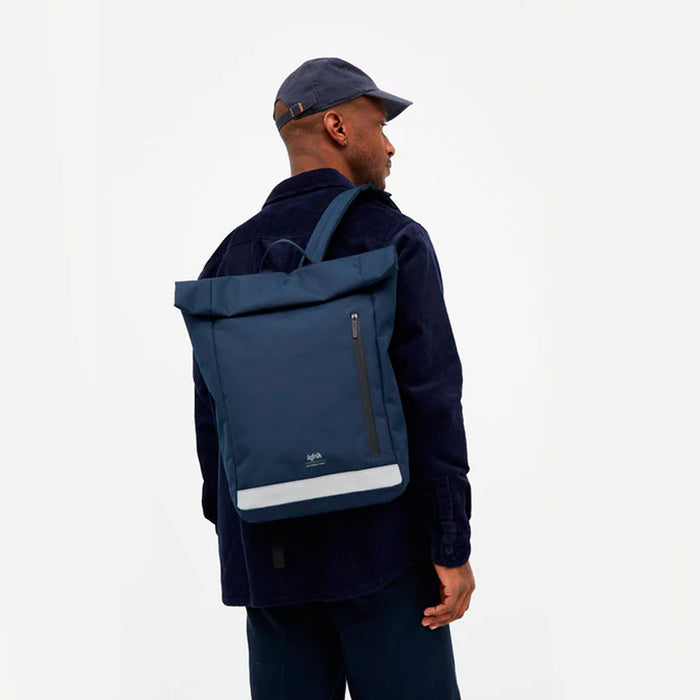 Mochila azul navy con banda reflectante de gran capacidad. Sistema de cierre mediante enrollado que permite pasar de 15 litros de capacidad a 19 litros de capacidad.