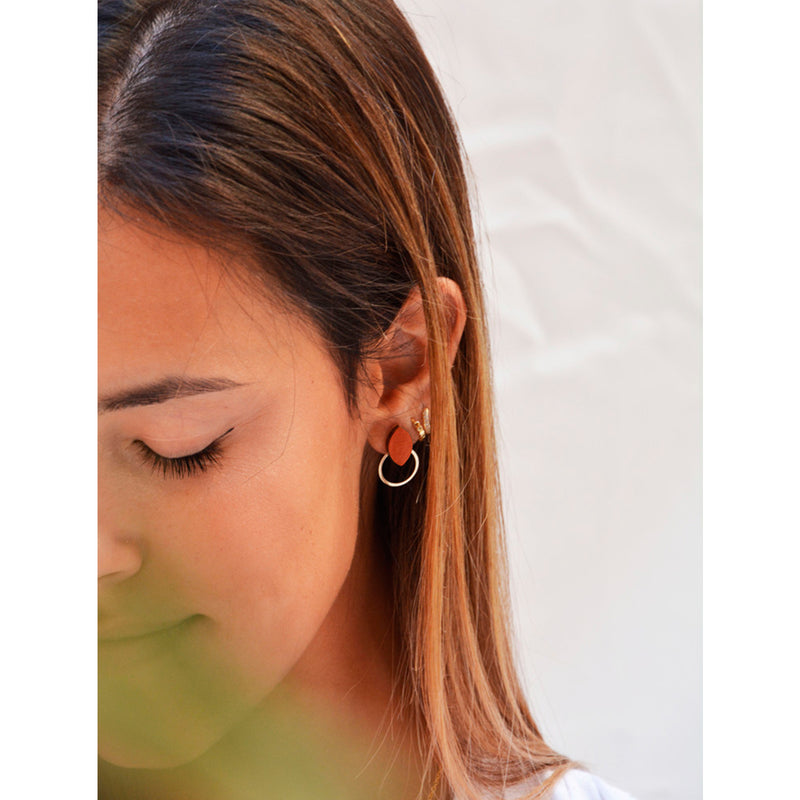 Modelo con Pendientes de madera con forma de hoja de olivo en color terracota  y aro plano dorado en la parte inferior.