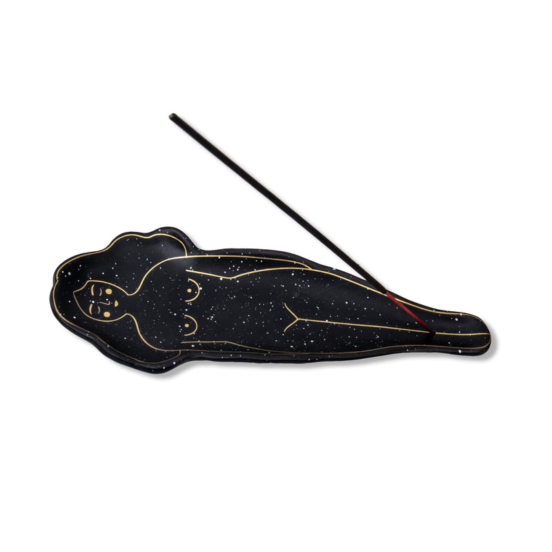 Bandeja para quemar barritas de incienso en forma de mujer tumbada. Bandeja portainciensos de color negro con motas plateadas y dibujo con líneas doradas.