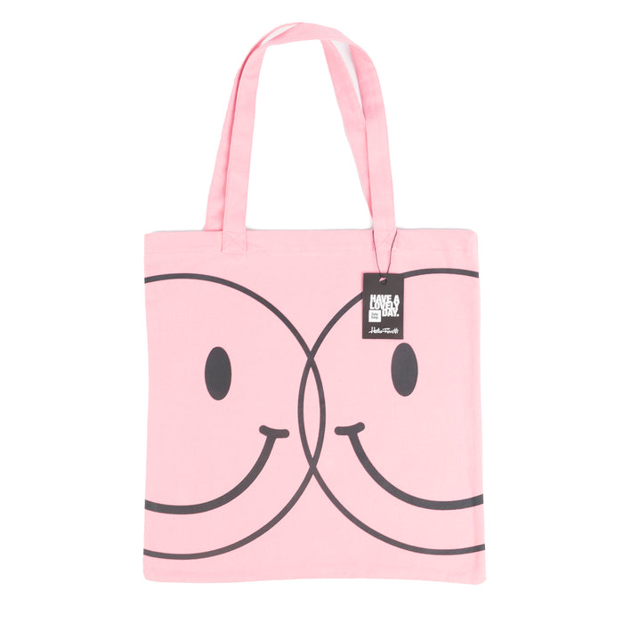 Tote bag color rosa con serigrafía de dos caritas sonrientes tipo smiley en color negro en una cara. 