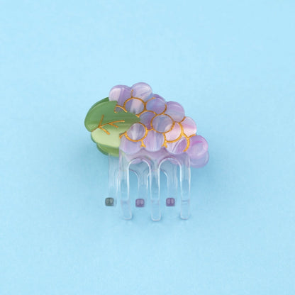 Pinza mini para el pelo en forma de racimo de uvas. Pinza original y divertida fabricada con acetato de celulosa reciclado y biodegradable. Vista lateral sobre fondo plano.